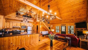 A spacious wooden cabin with a central dining area, kitchen, and a cozy living room with a fireplace. - New River Log Cabin | Waterfront • Sauna • Jet Tub (Pulaski County)