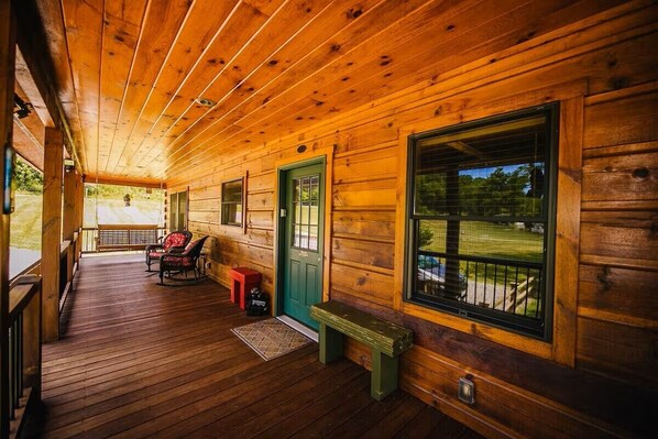 A wooden cabin with a porch, a green door, and a bench. - New River Log Cabin | Waterfront • Sauna • Jet Tub (Pulaski County)