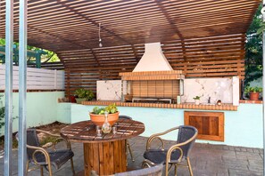 An outdoor patio with a round wooden table, two wicker chairs, a brick oven, and potted plants. - Dajana Apartments: Your Tranquil Home Base for Exploring Ksamil's Coast. (Ksamil)