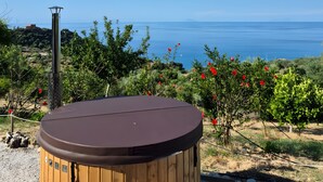 A hot tub with a wooden exterior, surrounded by a garden with red flowers and a view of the sea. - Bungalow 'Limone' with Sea View, Wi-Fi and Air Conditioning (Tusa)