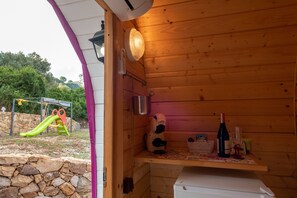 A wooden interior with a stone wall, a children's play area, a refrigerator, and a shelf with a bottle and glass. - Bungalow 'Limone' with Sea View, Wi-Fi and Air Conditioning (Tusa)
