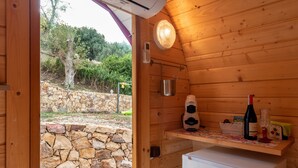 A wooden cabin with a stone wall outside, a small white refrigerator, a wine bottle, and a table with a decorative item. - Bungalow 'Limone' with Sea View, Wi-Fi and Air Conditioning (Tusa)