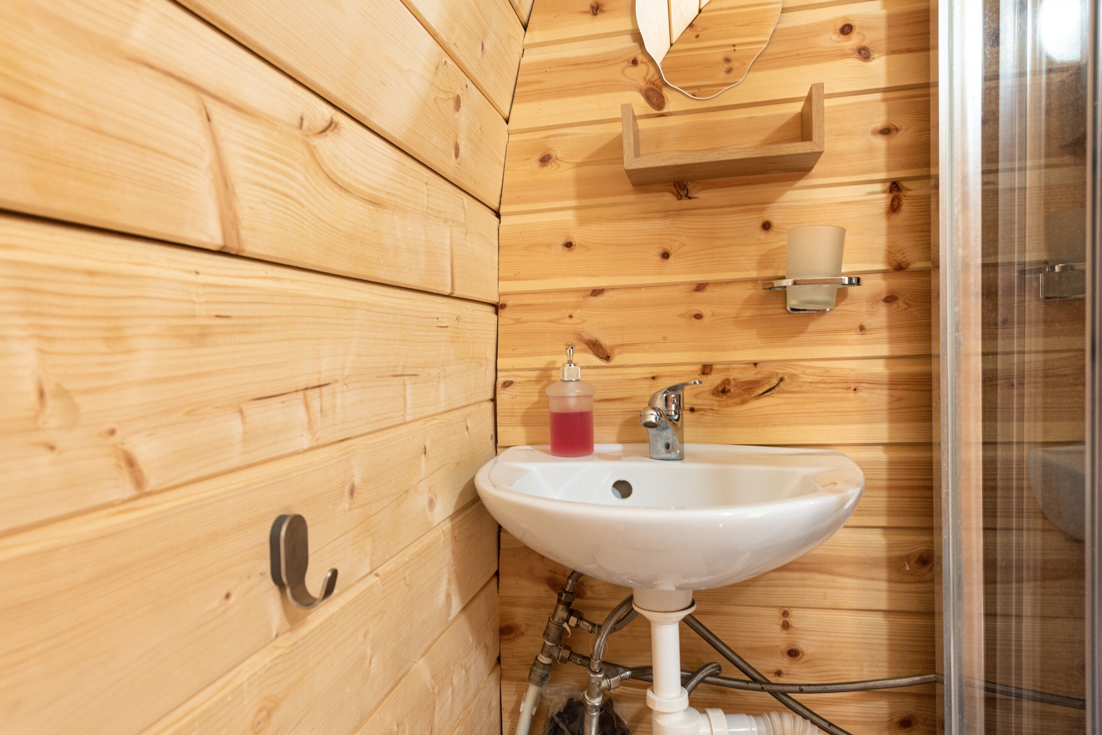 Un baño de madera con un lavamanos blanco, un espejo y una cabina de ducha.