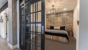 Un dormitorio con una cama grande, una pared de hormigón, una lámpara colgante y una puerta con manija metálica.