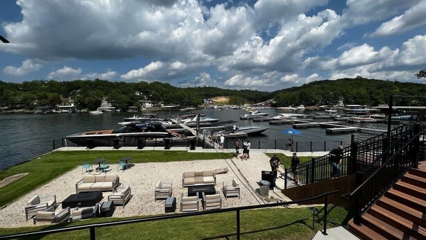 Un puerto deportivo con barcos amarrados, una zona verde con asientos al aire libre y vistas al agua y colinas al fondo.