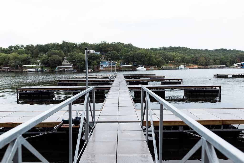 Un molo che conduce a un pontile con diverse imbarcazioni ormeggiate, circondato dall'acqua e da un pendio boscoso.