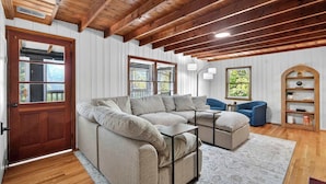 A cozy living room with a sectional sofa, a blue armchair, and a wooden ceiling. - Spacious cabin w/private river, hot tub & fire pit (Harpers Ferry)