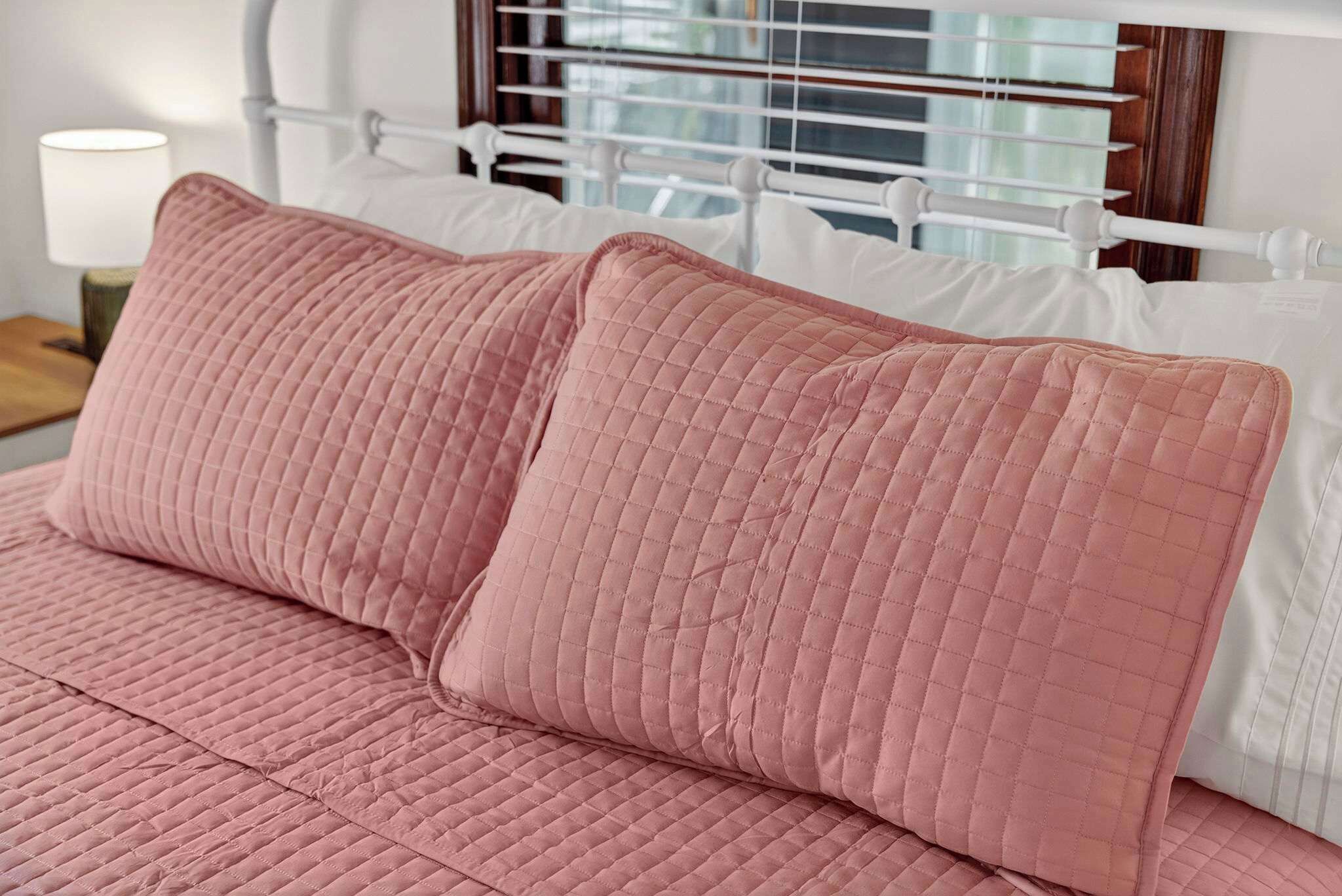 A bed with pink quilted bedding and white pillows.