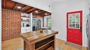 A kitchen with a brick wall, wooden ceiling beams, and a red door with a window. - Spacious cabin w/private river, hot tub & fire pit (Harpers Ferry)