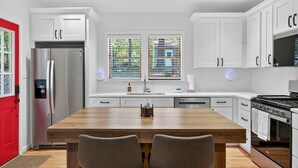 A modern kitchen with white cabinetry, a stainless steel refrigerator, a wooden dining table, and a built-in stove. - Spacious cabin w/private river, hot tub & fire pit (Harpers Ferry)