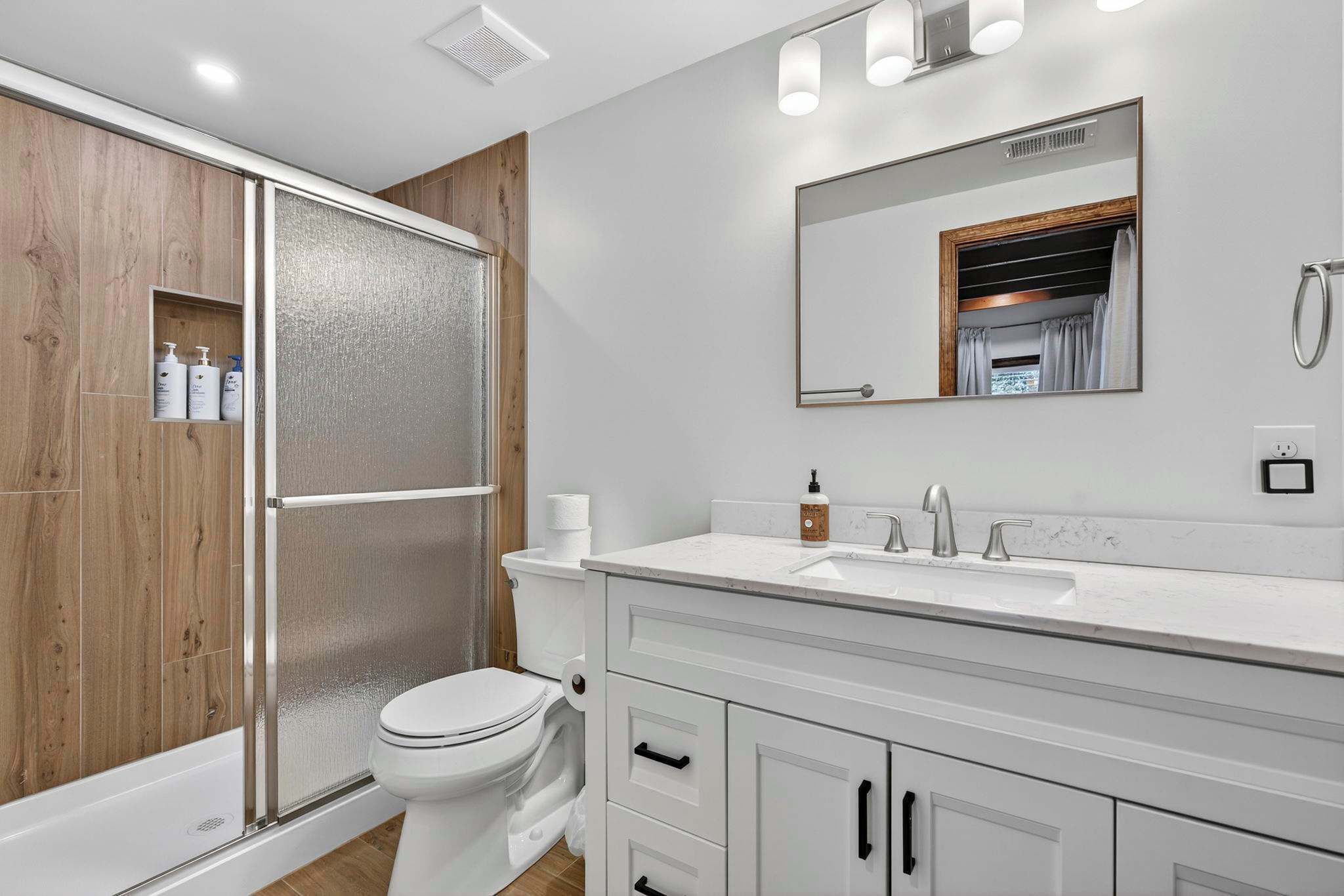 A modern bathroom with a shower enclosure, toilet, and vanity with a mirror.