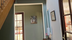 Un escalier menant à un balcon où se trouve un pot de fleurs, une porte avec un panneau de verre, un tableau encadré accroché au mur et un radiateur posé sur le sol.