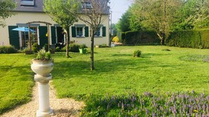 Un jardin bien entretenu, orné d’une colonne blanche, une maison aux volets verts et un ciel dégagé.