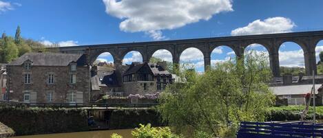 A stone bridge with multiple arches over a river, with buildings and a bench in the foreground.