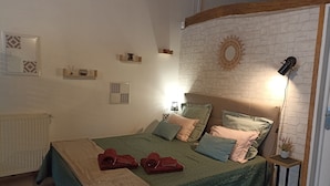 Ein Schlafzimmer mit einem Bett, einem Nachttisch, einer Lampe und einer Wand mit dekorativem Spiegel und Wandbildern.