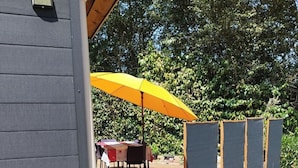 Ein überdachter Außenbereich mit gelbem Sonnenschirm, einem Tisch mit Stühlen und einer Holzterrasse.