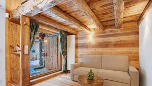 A wooden interior with a sofa, a small round table, and a window with curtains.