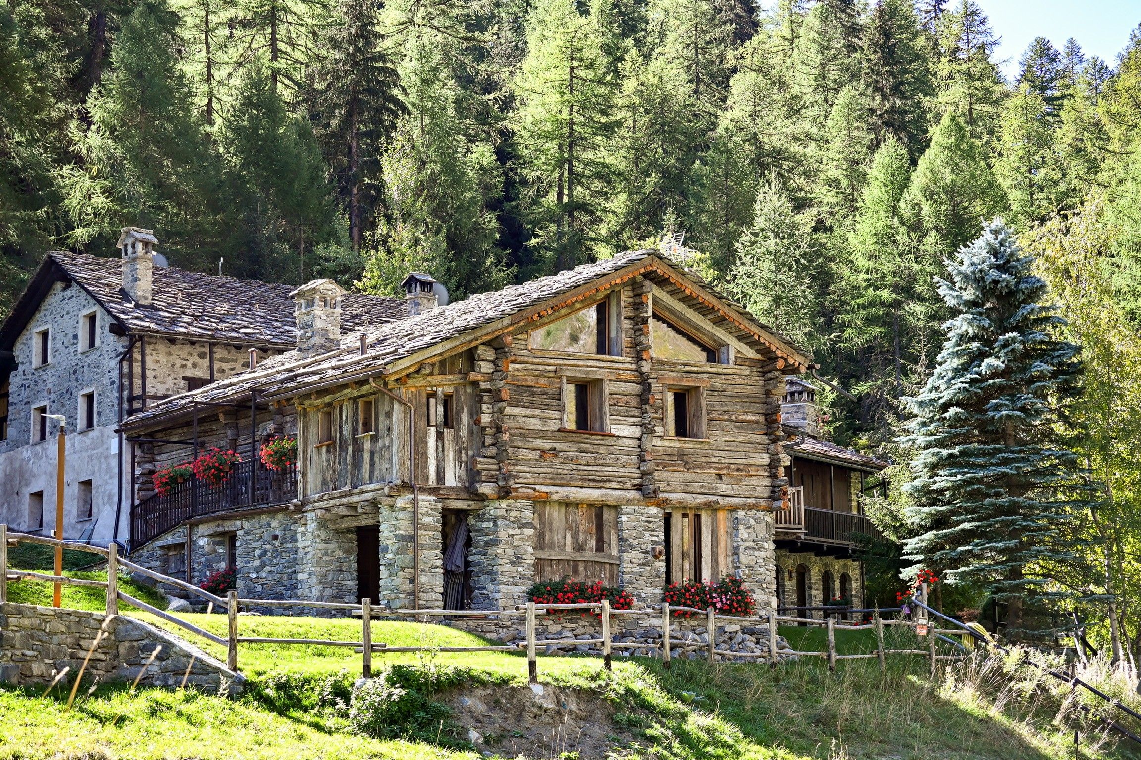 A traditional stone building with a sloped roof, wooden balconies, and a stone staircase leading to the entrance.