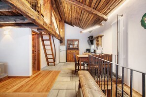 Ein rustikaler Innenraum mit freiliegenden Holzbalken, einer Holztreppe, einem Essbereich und einer Küche.