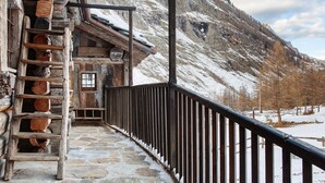 A wooden staircase leading to a door, a stone-paved path, and a mountain backdrop.