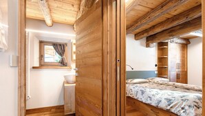 Interior de madeira com uma cama, uma janela com cortinas, um armário de madeira e um radiador.