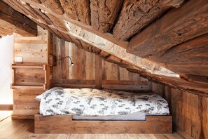Een houten hoogslaper met schuine wanden, ingebouwde opbergruimte en een bed met een decoratief sprei.