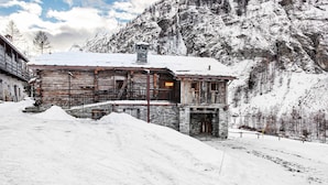 Um edifício rústico de madeira com escadaria de pedra, rodeado por montanhas cobertas de neve.