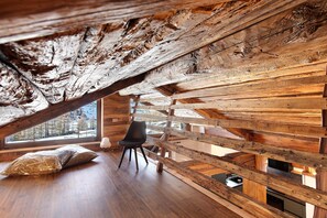 Un interior rústico de madera con techo inclinado, una silla negra y un ventanal con vista a árboles.