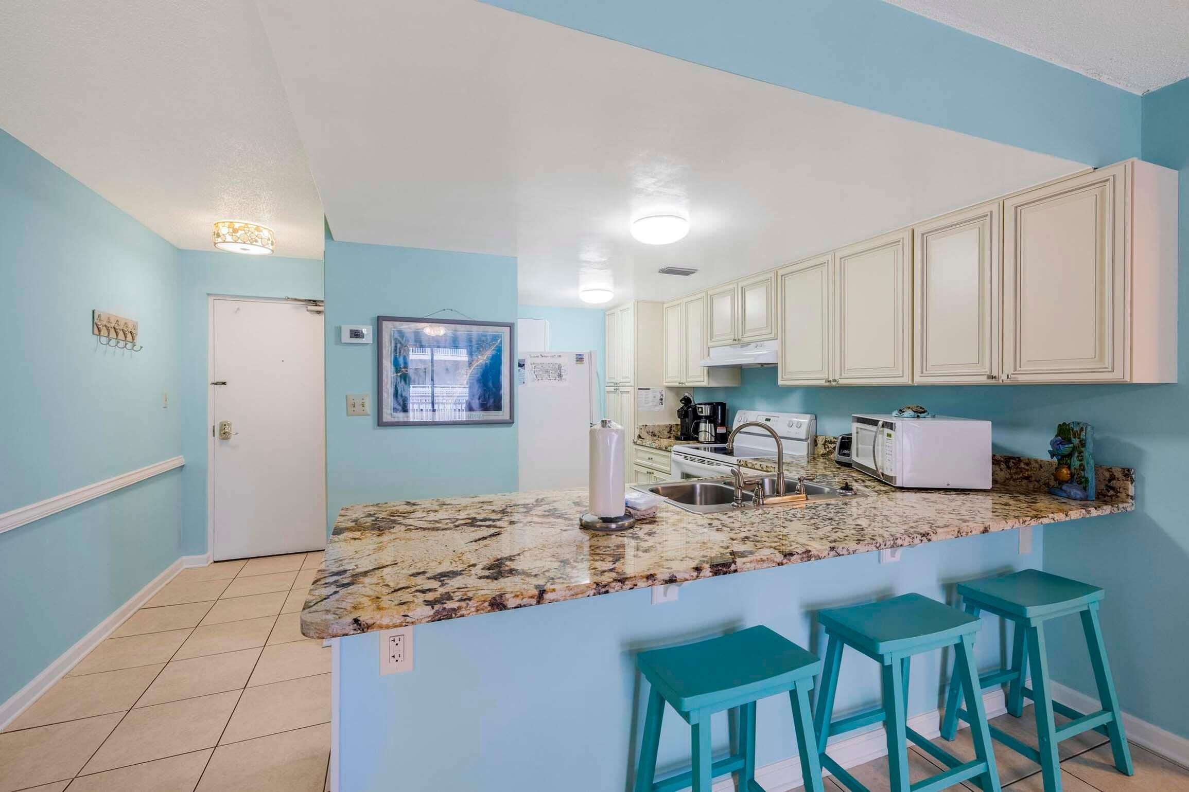 A kitchen with a granite countertop, white cabinets, and teal bar stools.
