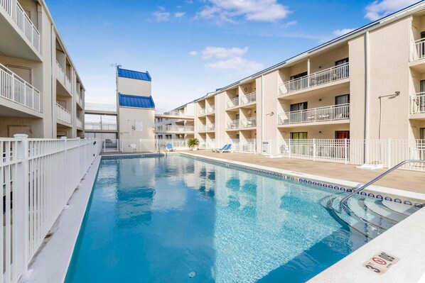 A swimming pool surrounded by multi-story buildings with balconies, a clear sky, and a blue sky. - Sugar Beach 132 (Orange Beach)
