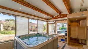 Ein Whirlpool in einem Zimmer mit großen Fenstern, Holzbalken und Blick auf einen Pool im Freien.