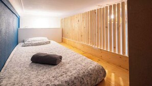 A room with a wooden slat wall, a bed with floral bedding, and a window with sunlight. - Bright apartment close to the city center (Nîmes)