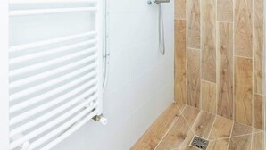 A shower area with a white radiator, a wooden wall, and a tiled floor. - Bright apartment close to the city center (Nîmes)