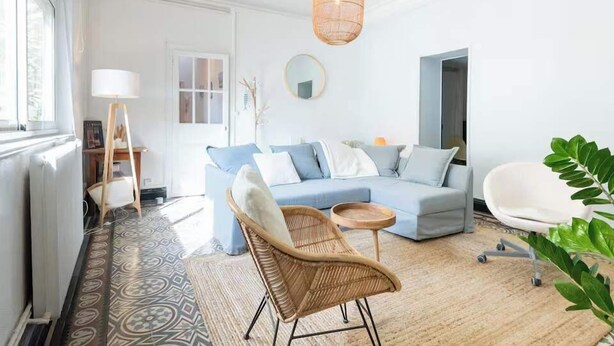 A modern living room with a blue sofa, a wicker chair, a round table, and a hanging light fixture. - Bright apartment close to the city center (Nîmes)