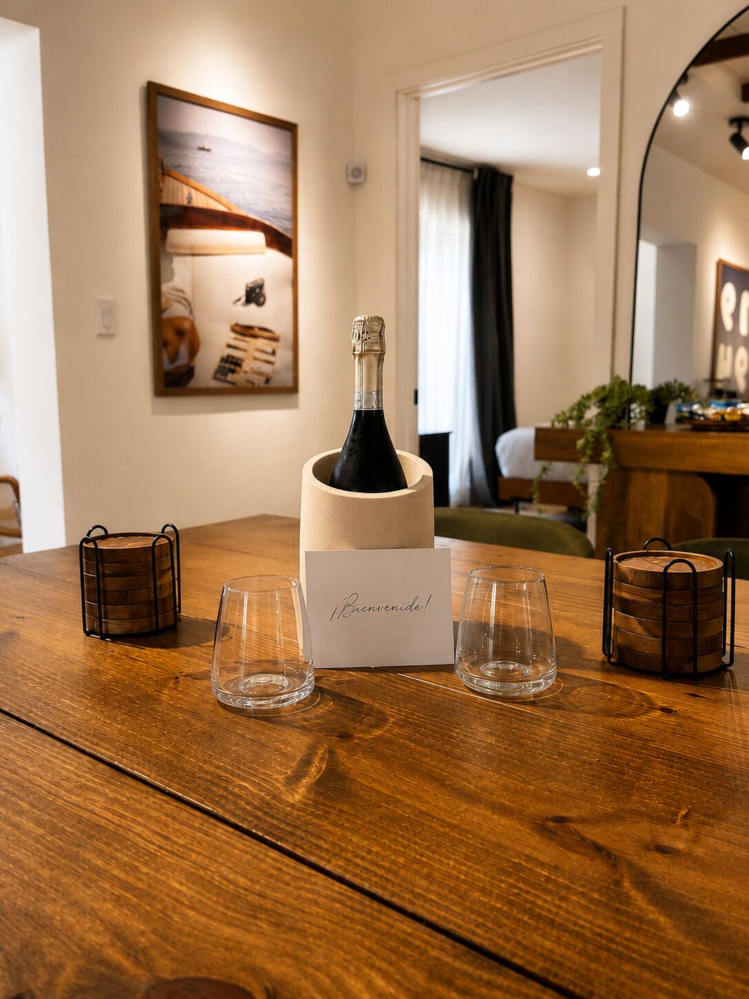 Ein Holztisch mit einer Champagnerflasche, zwei Gläsern und einer 'Bienvenidos!'-Karte.