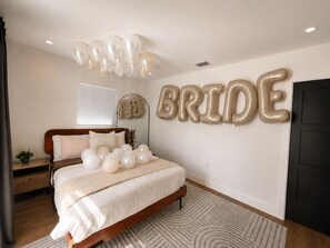 Ein Schlafzimmer mit einem Bett, Ballons und einer Wanddekoration mit dem Schriftzug 'BRIDE'.