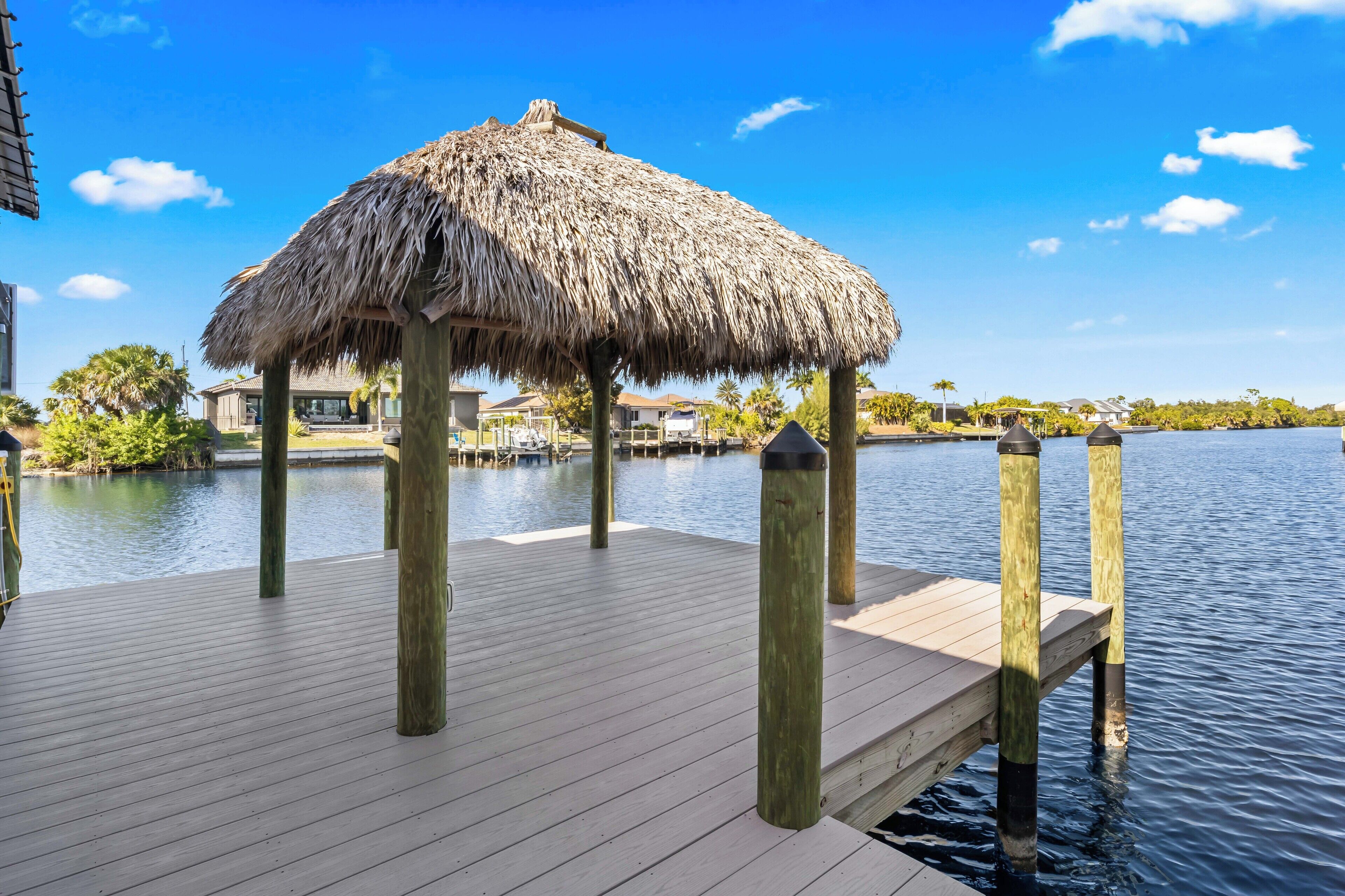 A wooden dock with a thatched roof structure, surrounded by calm water and greenery.