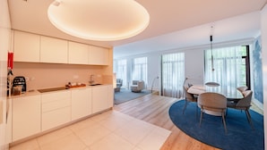 A modern kitchen with white cabinets, a dining area with a round table and chairs, and a large window providing natural light. - Bolhão Prime | Luxe 3BR + Garage (Oporto)
