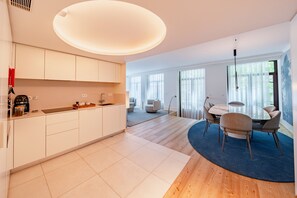 A modern kitchen with white cabinets, a dining area with a round table and chairs, and a large window providing natural light. - Bolhão Prime | Luxe 3BR + Garage (Oporto)
