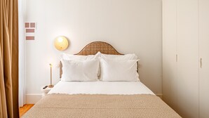 A neatly made bed with a headboard, a bedside lamp, and a wall-mounted light fixture. - Bolhão Prime | Luxe 3BR + Garage (Oporto)