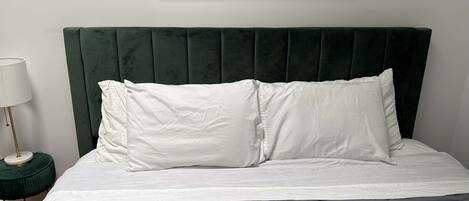 A bed with a green upholstered headboard, white pillows, and a gray quilted bedspread.