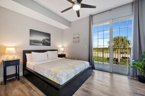 A modern bedroom with a large bed, two bedside lamps, a ceiling fan, and a view of the outdoors through a sliding glass door. - Waterfront 3B Townhome | Beach Access & Hot Tub! (Ruskin)