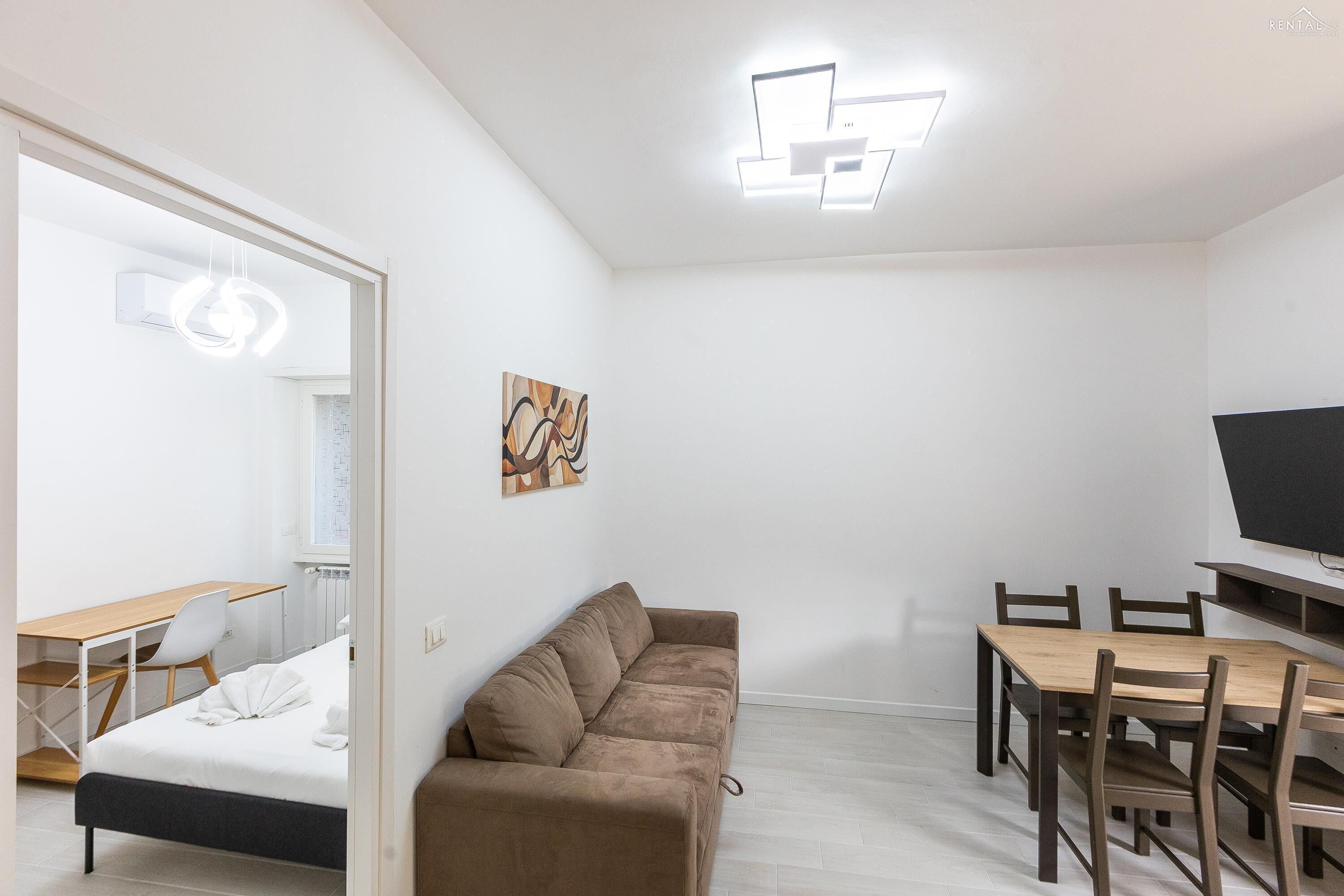 A modern, minimalist room with a brown sofa, a wooden dining table, and a TV.