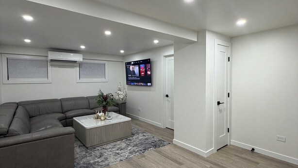 A modern living room with a sectional sofa, a coffee table, and a flat-screen TV mounted on the wall.