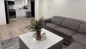 A modern living room with a grey leather sofa, a white marble coffee table with a Christmas tree and ornaments, and a kitchen in the background.