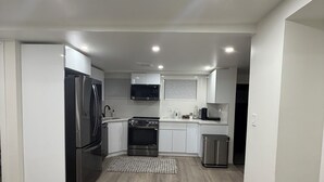 A modern kitchen with white cabinets, stainless steel appliances, and a wooden floor.