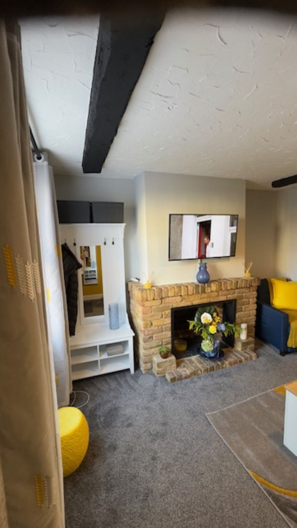 Una sala de estar con chimenea, un armario blanco, un reposapiés amarillo y un sofá azul.