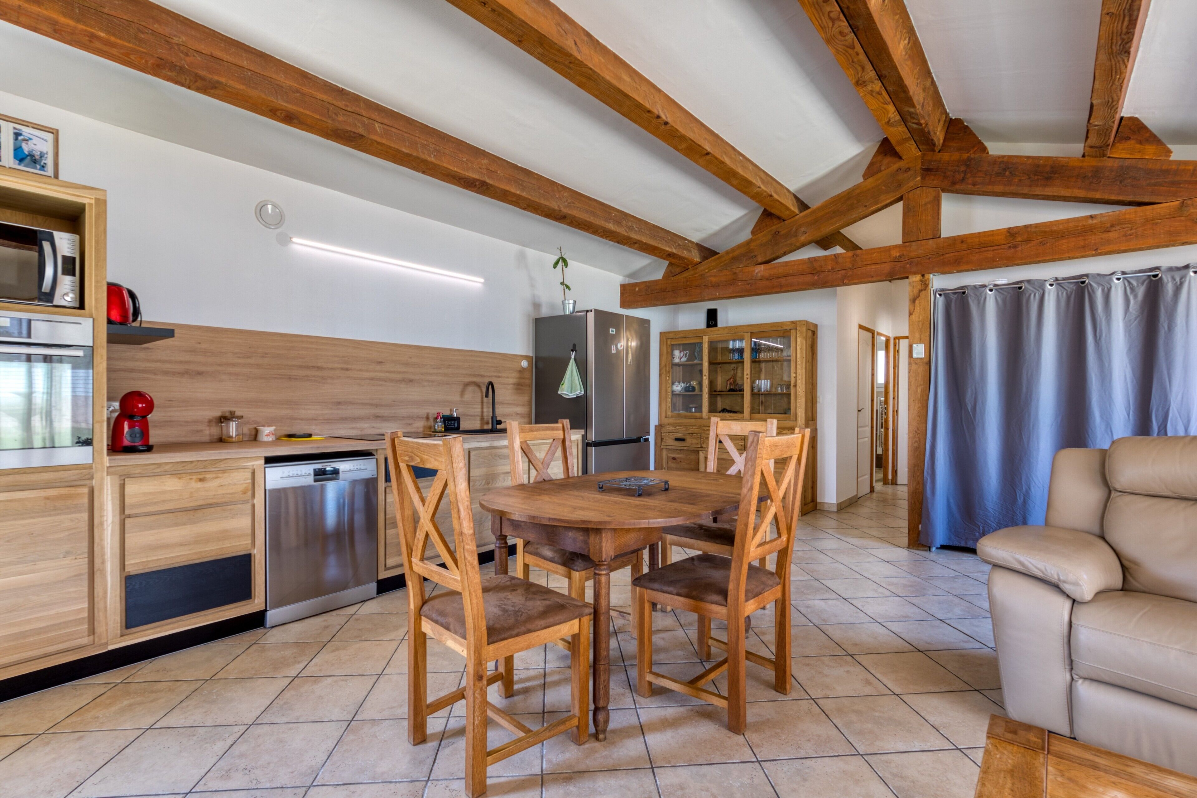A kitchen with wooden cabinets, a dining table with chairs, a refrigerator, and a coffee maker.