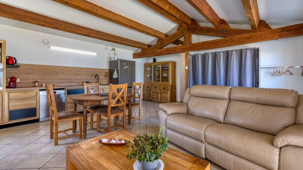 Una cocina moderna con vigas de madera, un comedor con mesa y sillas, y un sofá de cuero color beige.