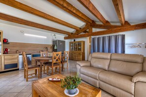 A modern kitchen with wooden beams, a dining area with a table and chairs, and a beige leather sofa. - Holiday Home 'Villa En Camargue' with Shared Pool, Wi-Fi and Air Conditioning (VAUVERT)